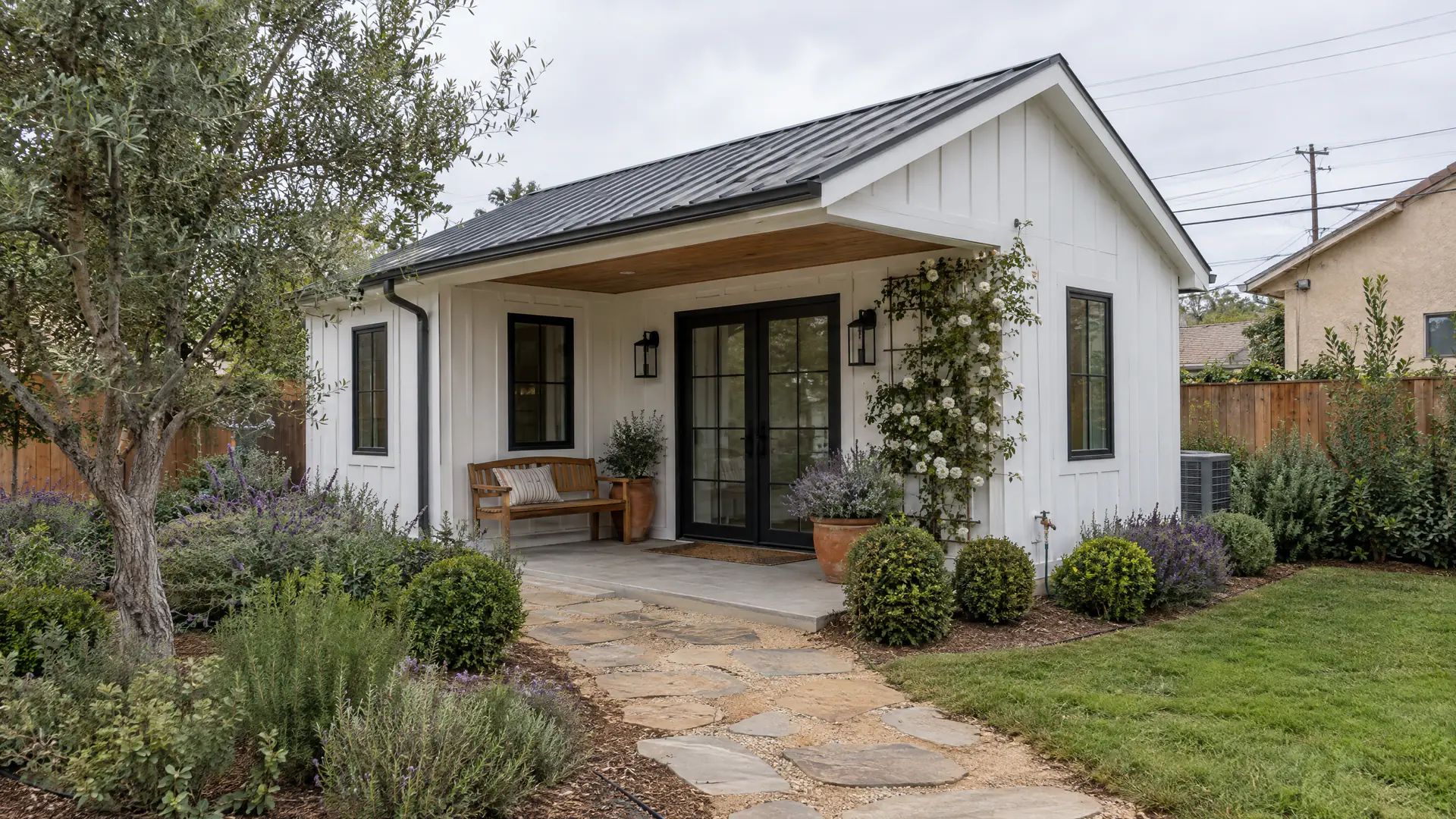 Detached backyard ADU cottage with white board-and-batten siding and a garden path
