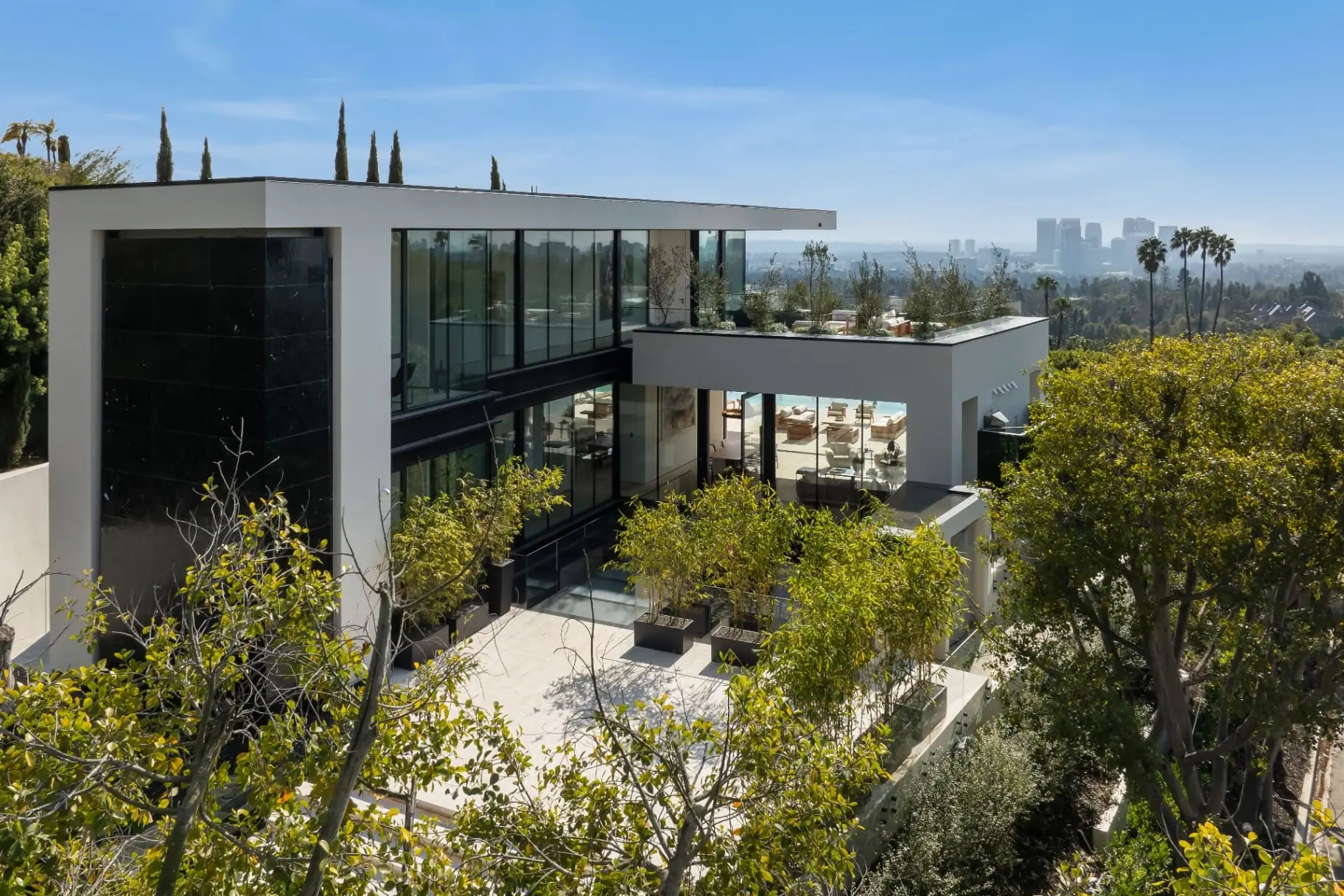 Glass-walled upper floor and planted terrace of the Laurel Way custom home in Beverly Hills, built by Valley Vista Builders, with the city skyline in the distance