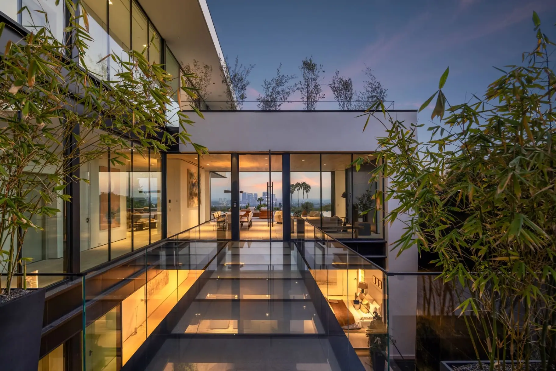 Glass-floored skybridge at dusk leading to the glass-walled dining and living area of the Laurel Way custom home, built by Valley Vista Builders