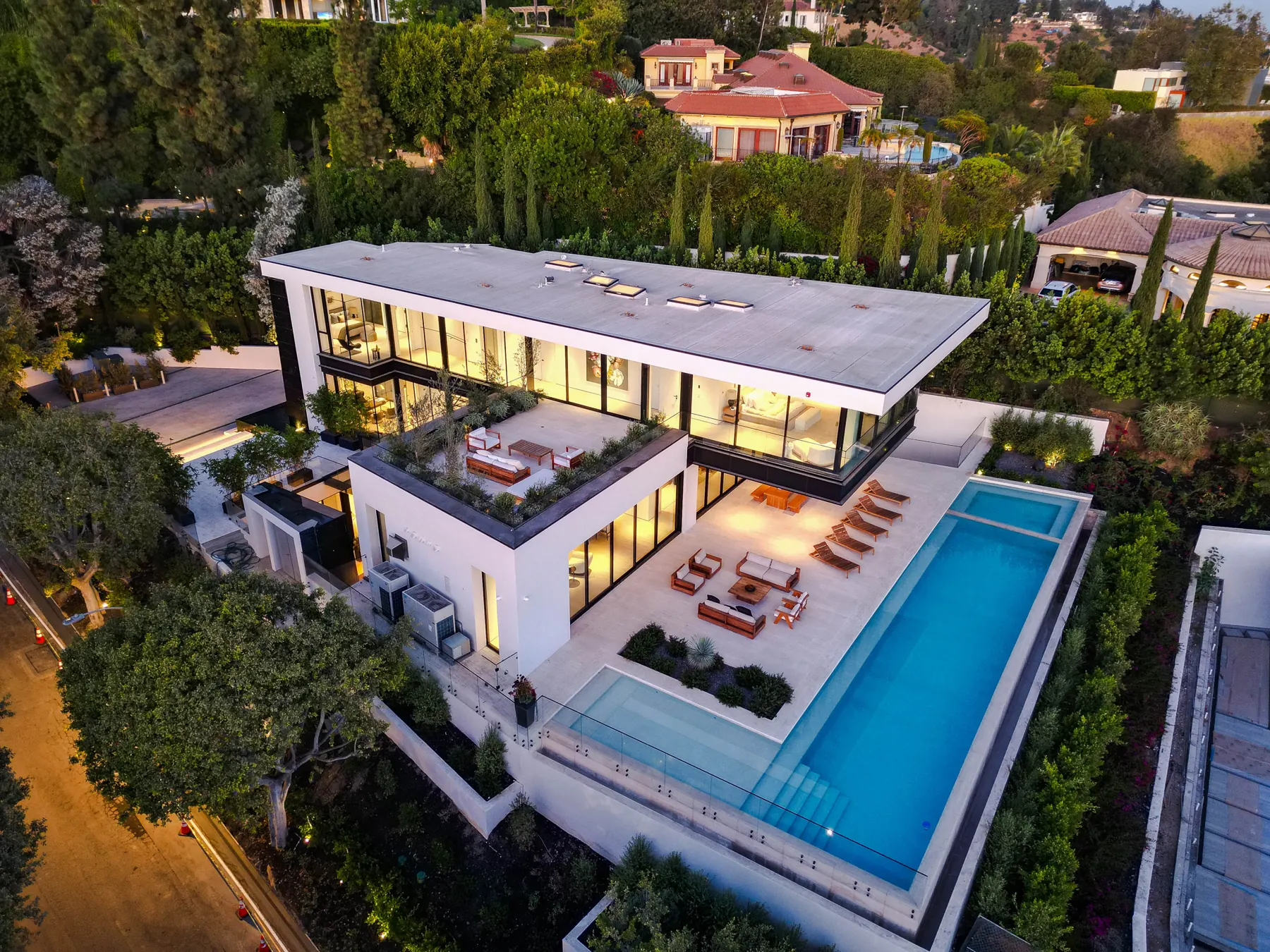Aerial view at dusk of the flat-roofed house and long infinity pool at the Laurel Way custom home in Beverly Hills, built by Valley Vista Builders