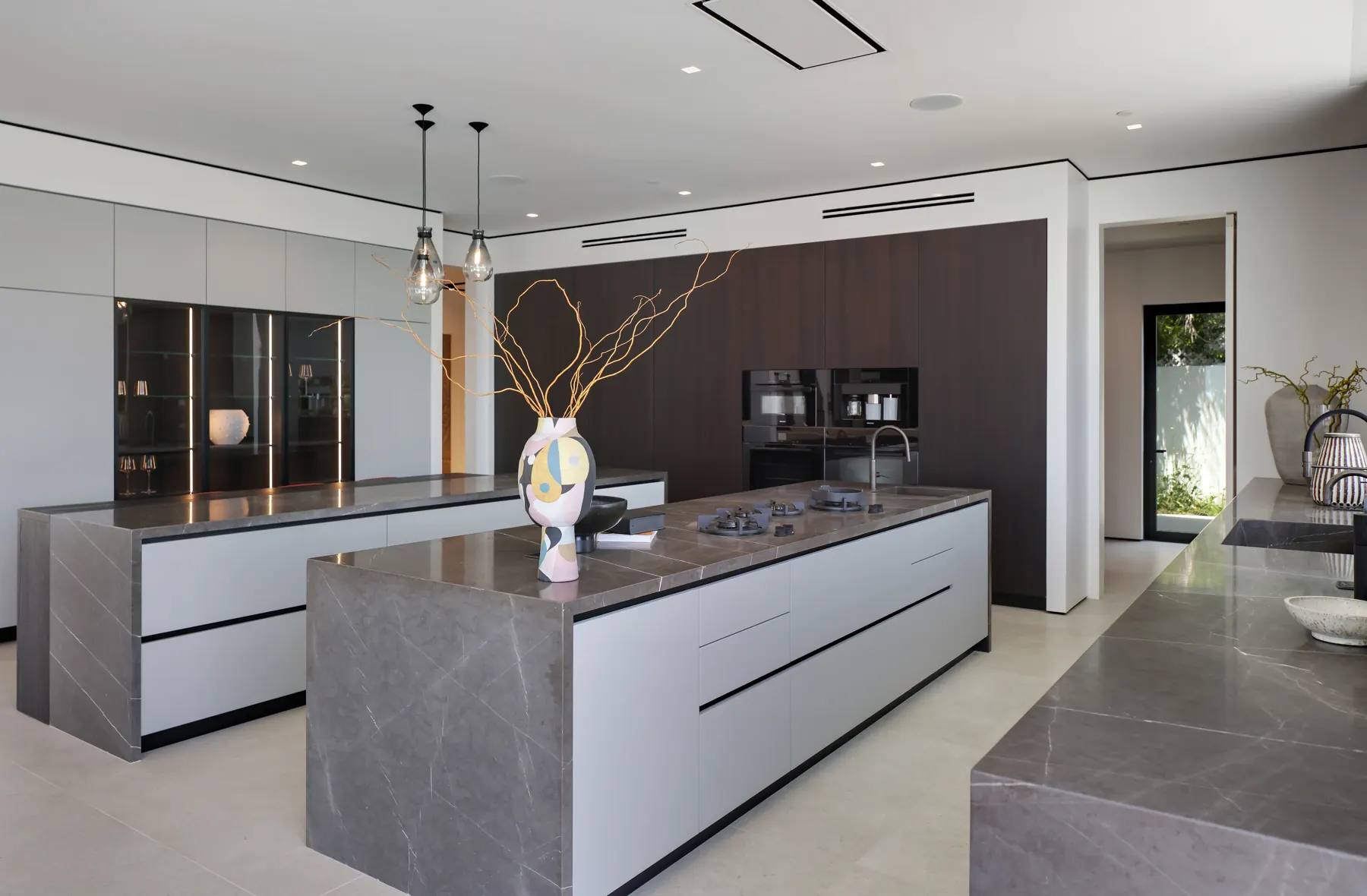 Kitchen with stone-topped islands and dark wood cabinetry at the Laurel View Residence, a Hollywood Hills home built by Valley Vista Builders